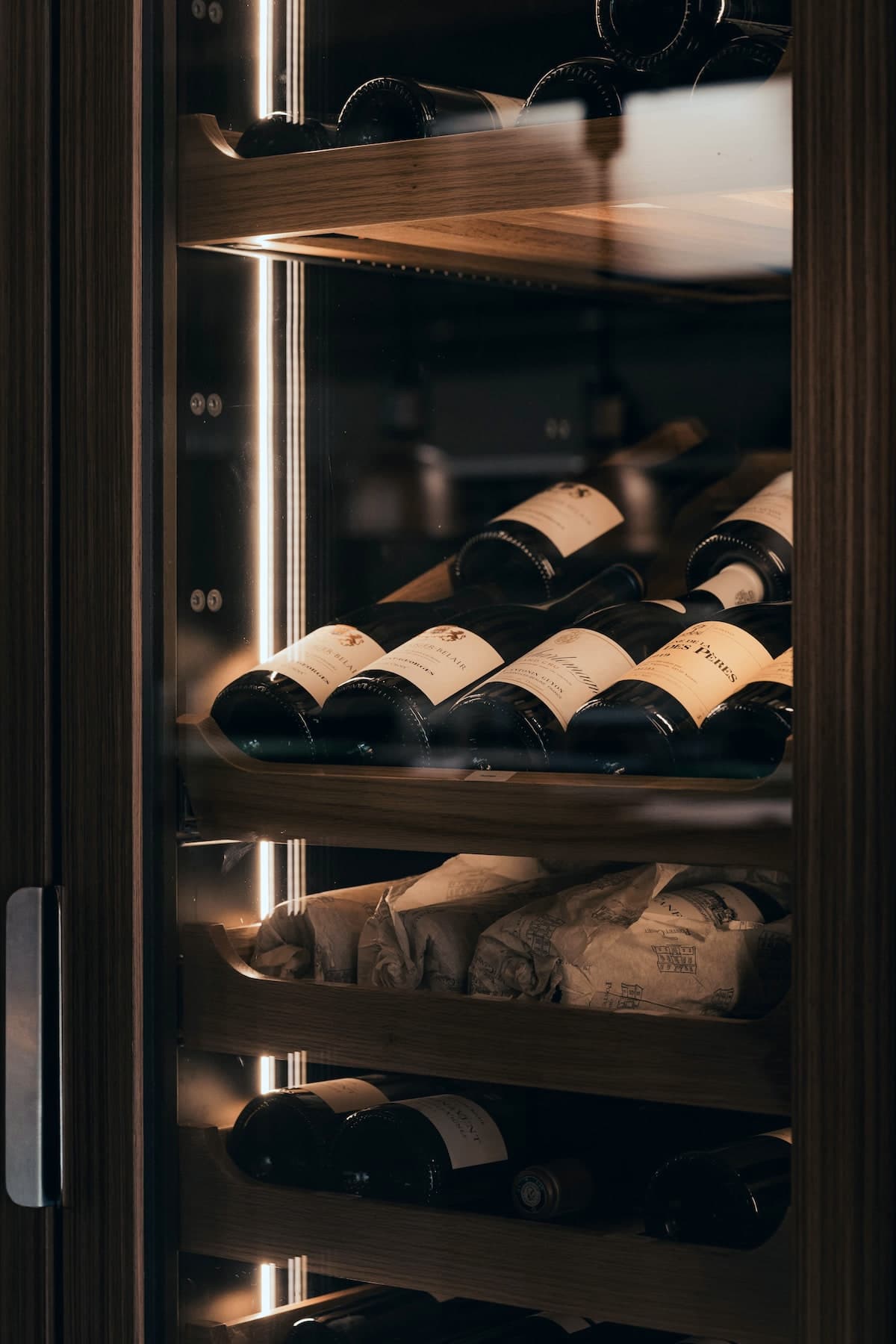 Armoire à vin en bois sombre, étagères rétroéclairées et bouteilles couchées derrière la porte vitrée