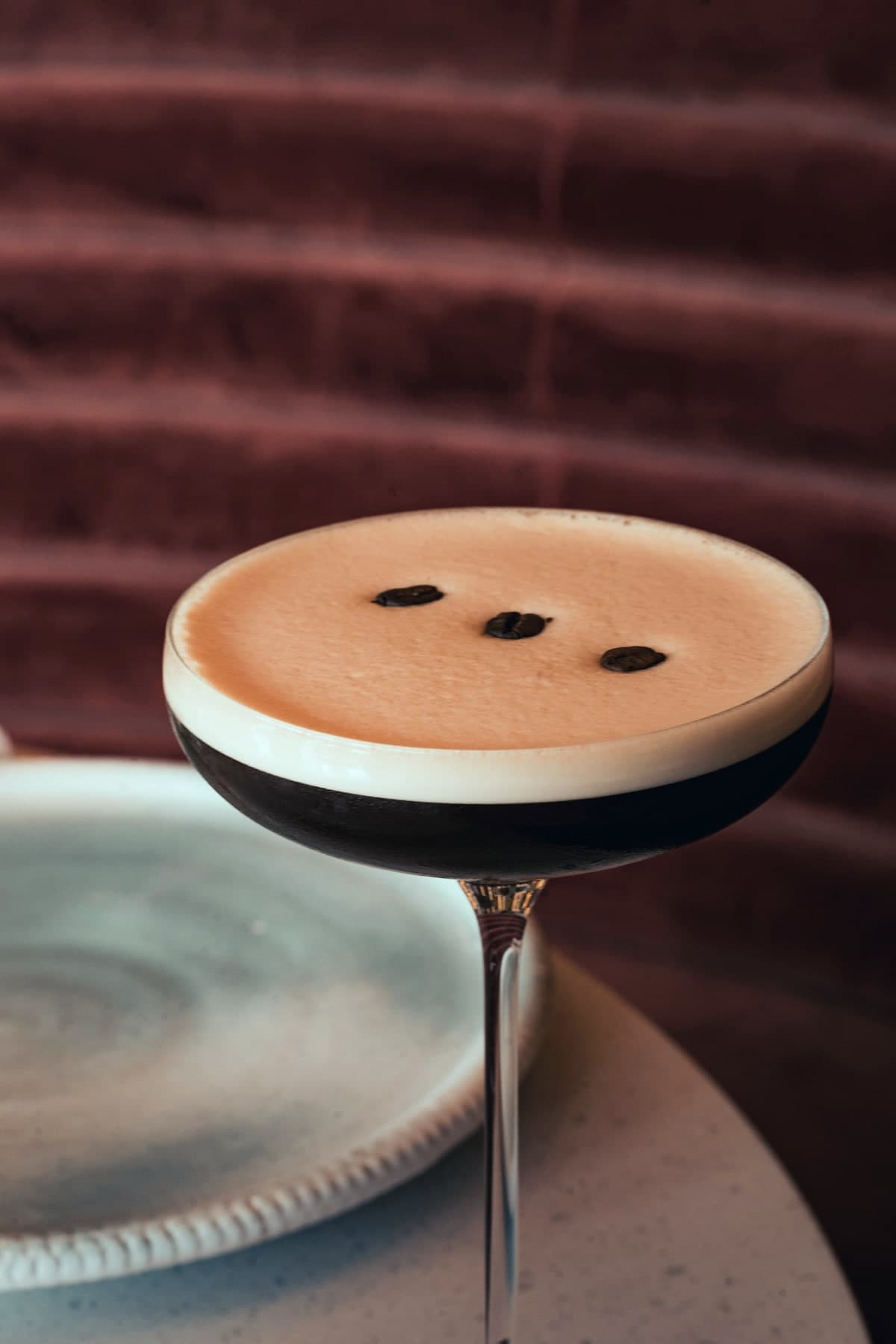 Espresso martini en coupe, trois grains de café posés sur la mousse, devant une banquette de velours