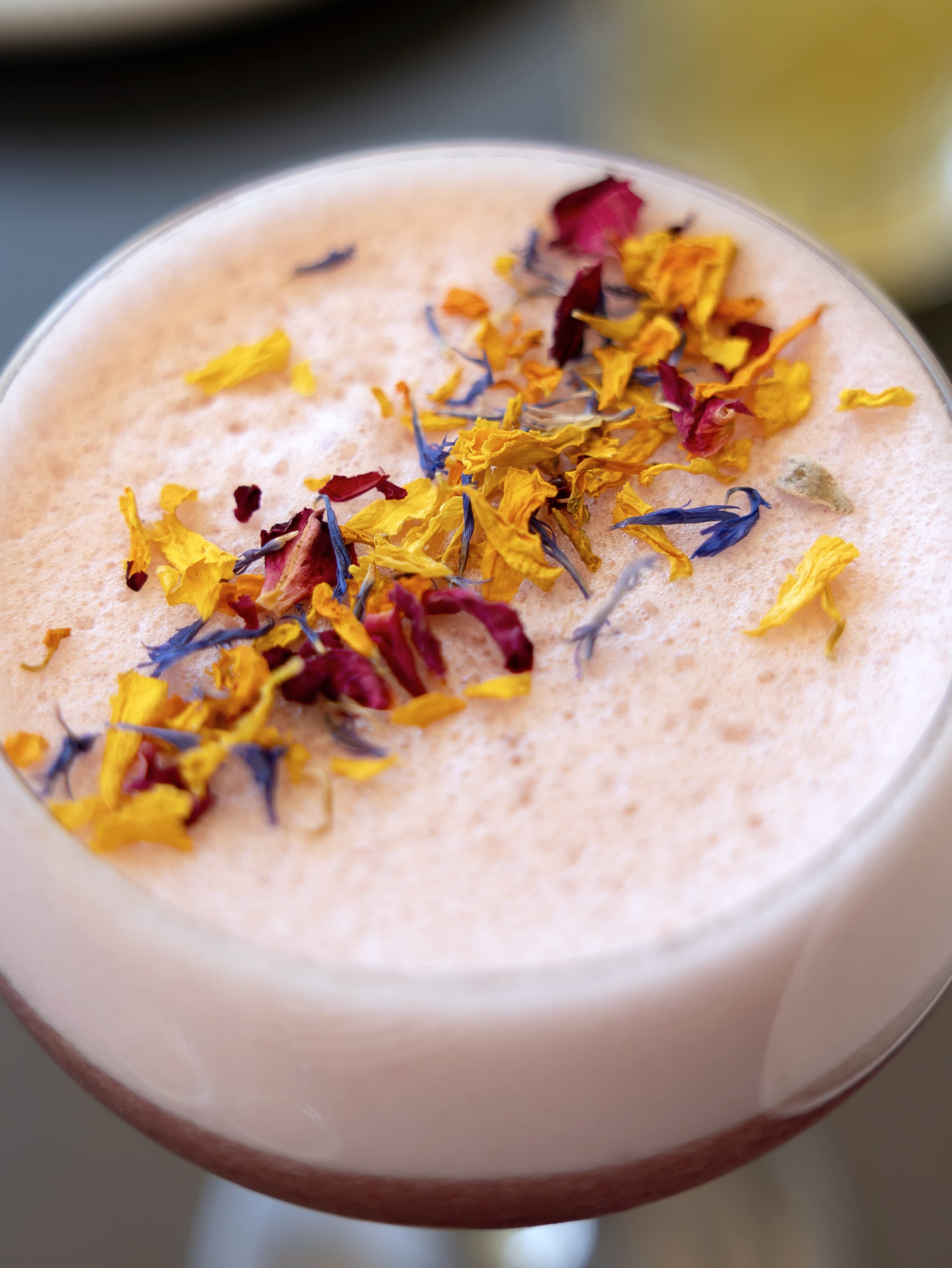 Cocktail rose en coupe, mousse couverte de pétales de fleurs séchées jaunes, bleus et rouges