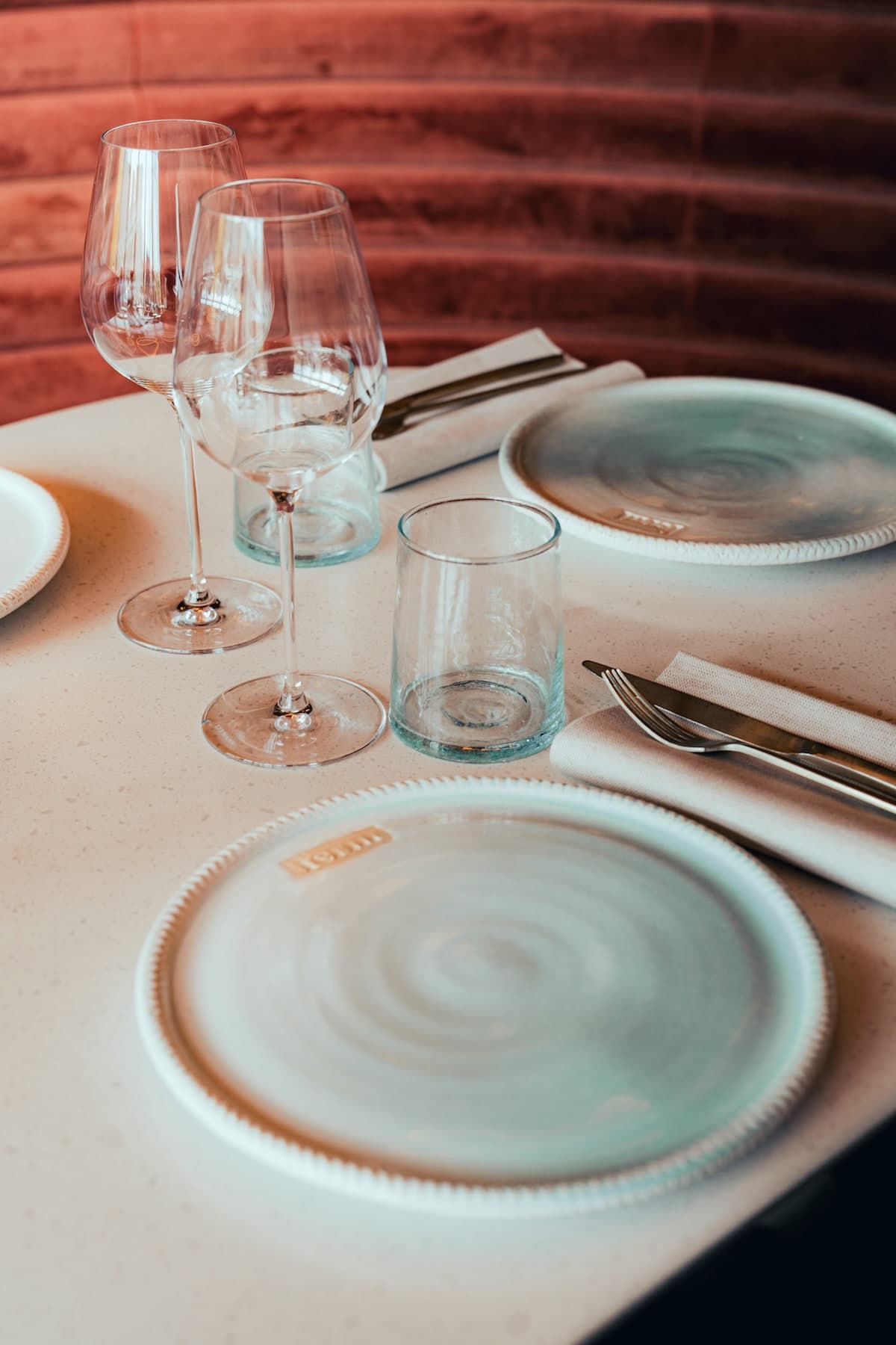 Couvert dressé sur une table de terrazzo rose : assiettes de grès signées Ferni, deux verres à vin et un verre à eau