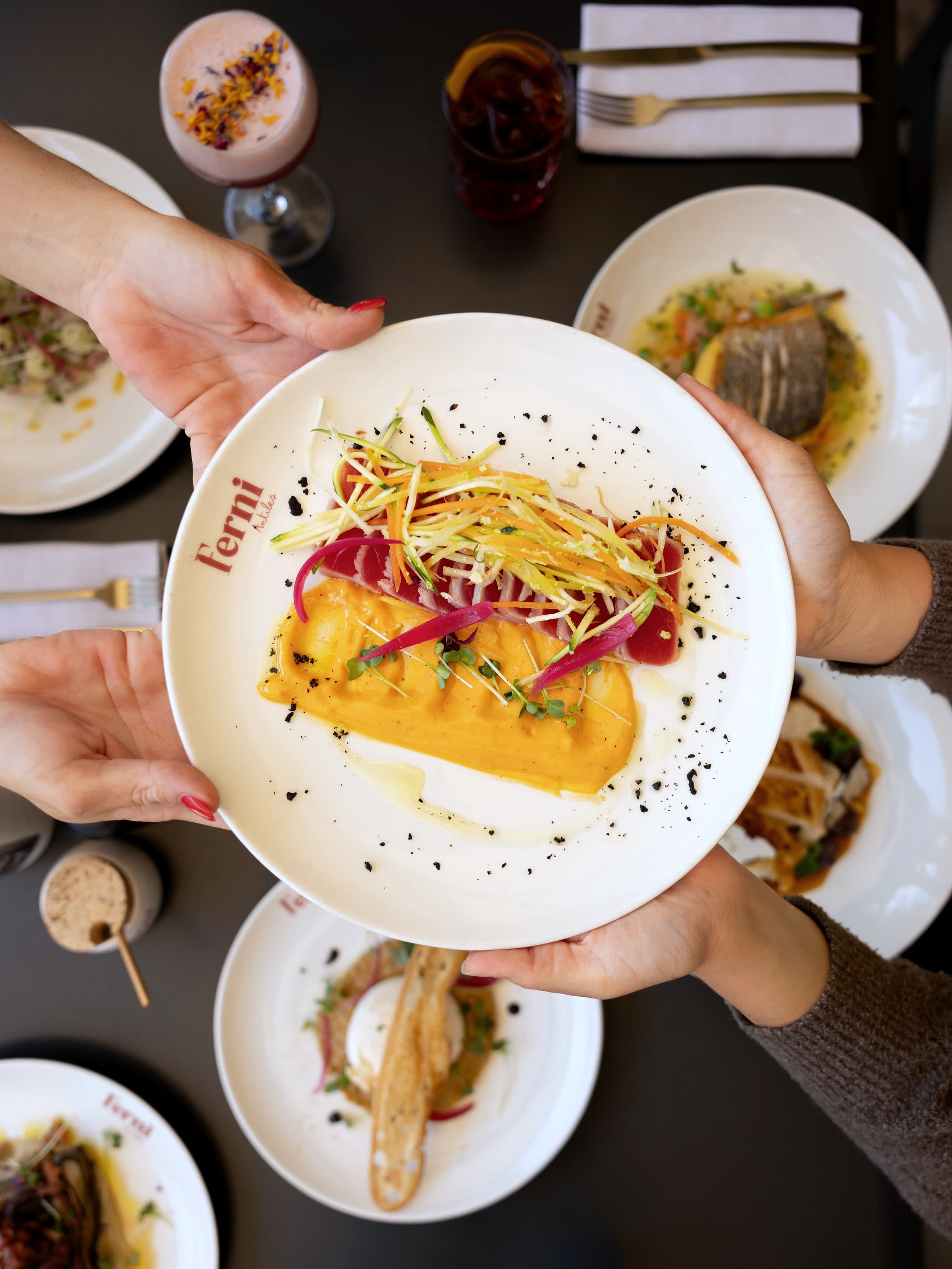 Deux mains présentent une assiette de poisson couverte de julienne de légumes et de graines de sésame noir