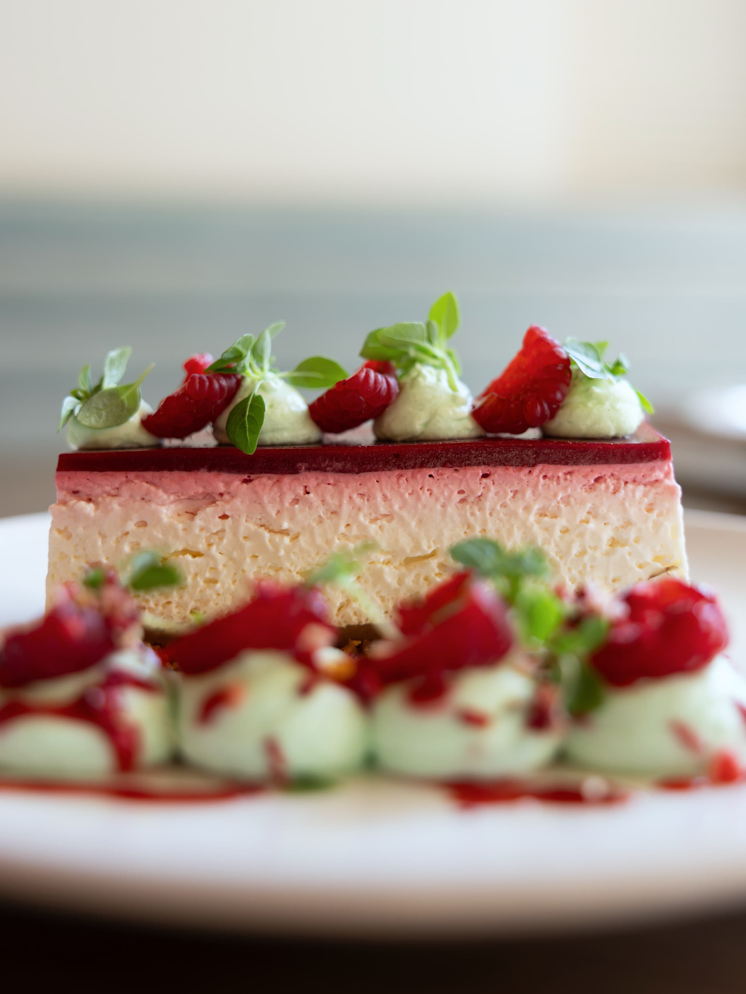 Entremets à la fraise coupé net, mousse claire, gelée rouge et quenelles de crème pistache sur le dessus