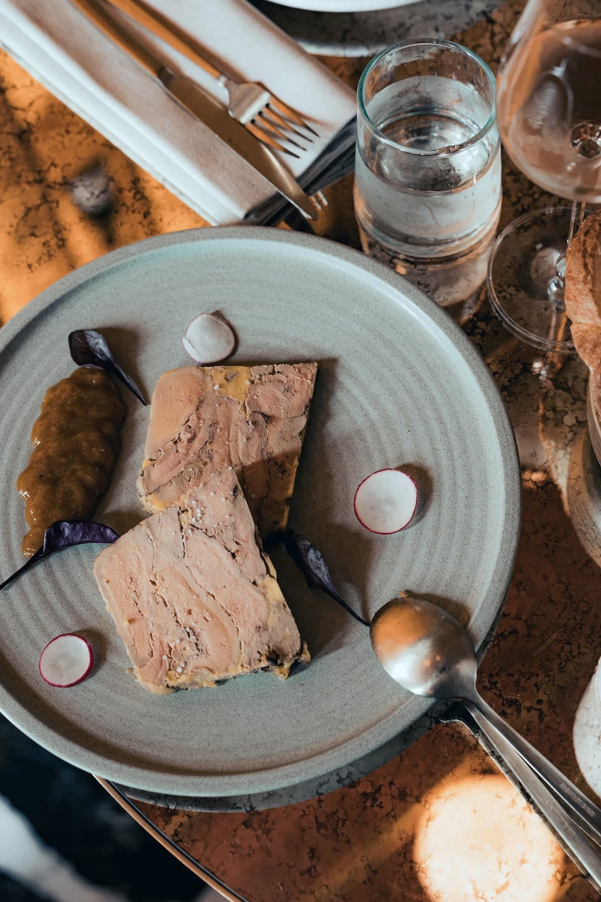 Deux tranches de terrine de foie gras vues de dessus, chutney, radis roses et oignon rouge sur une assiette de grès