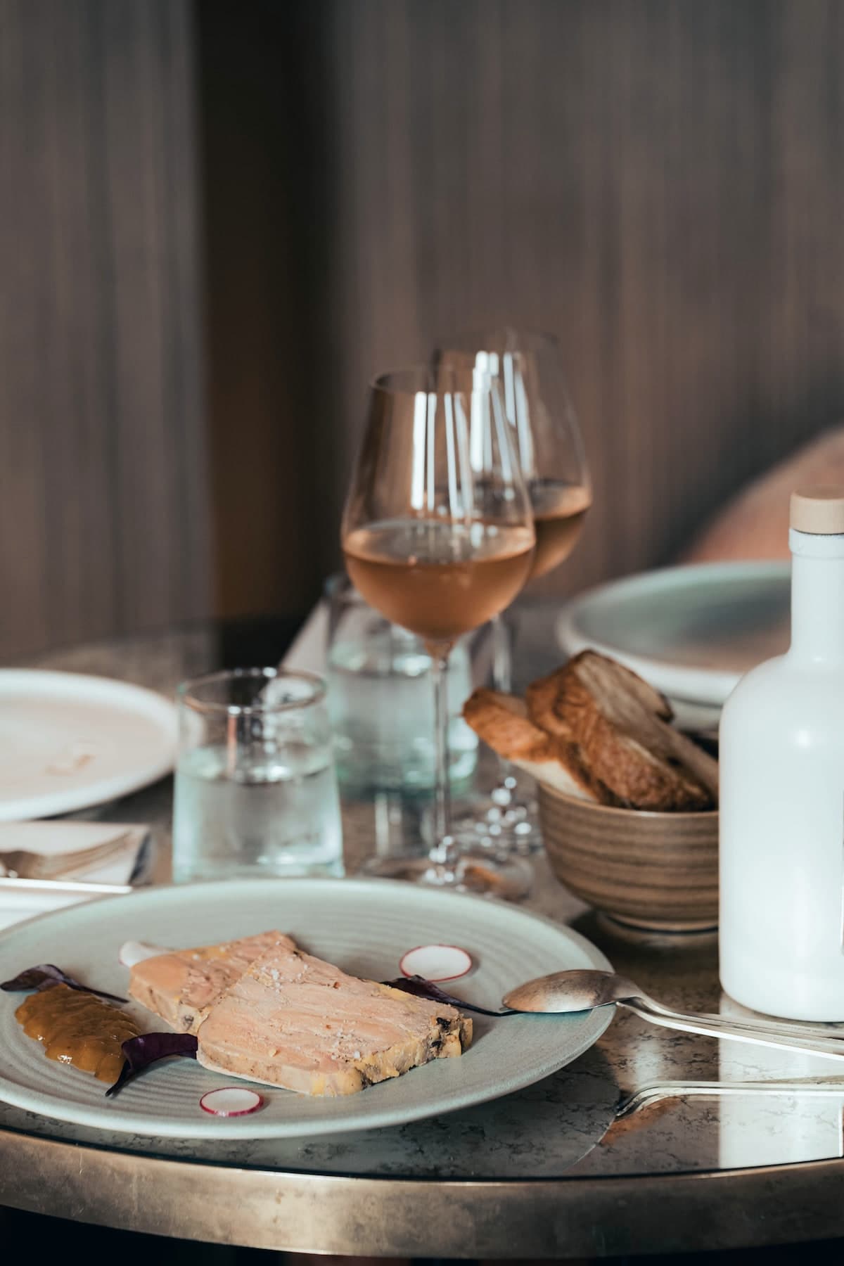 Assiette de foie gras sur un guéridon de laiton, deux verres de rosé, une corbeille de pain grillé et une carafe blanche