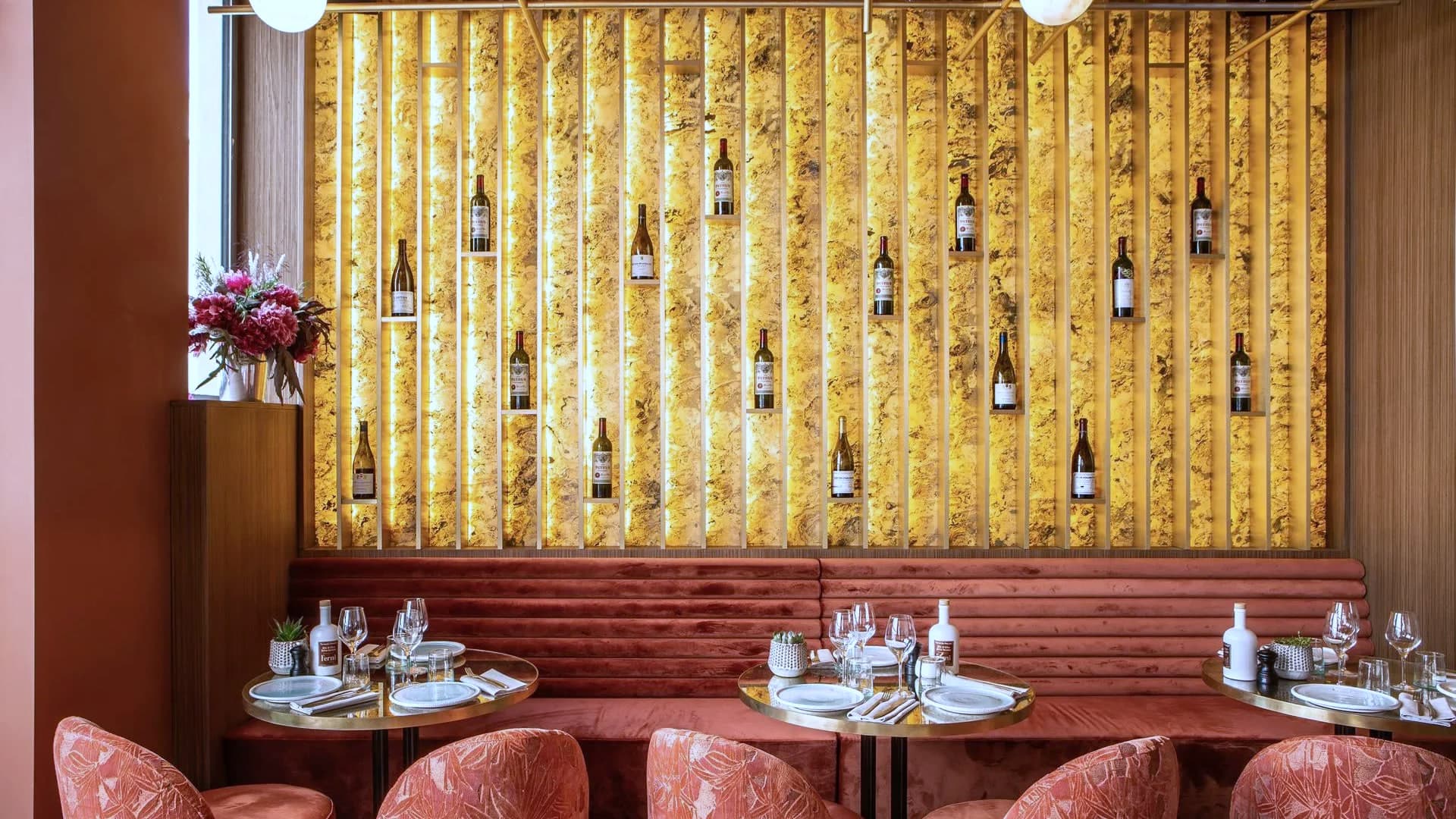 Mur d’onyx doré rétroéclairé portant une vingtaine de bouteilles, devant une banquette cannelée terracotta