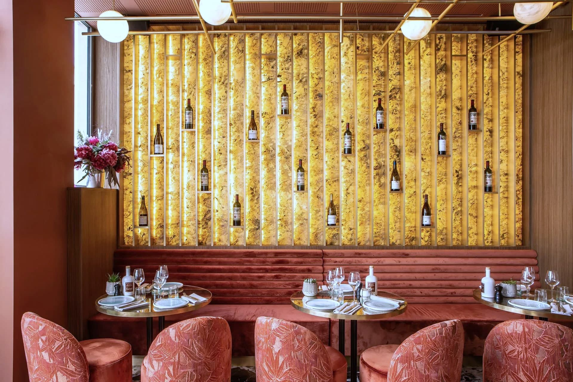 Mur d’onyx doré rétroéclairé portant une vingtaine de bouteilles, devant une banquette cannelée terracotta