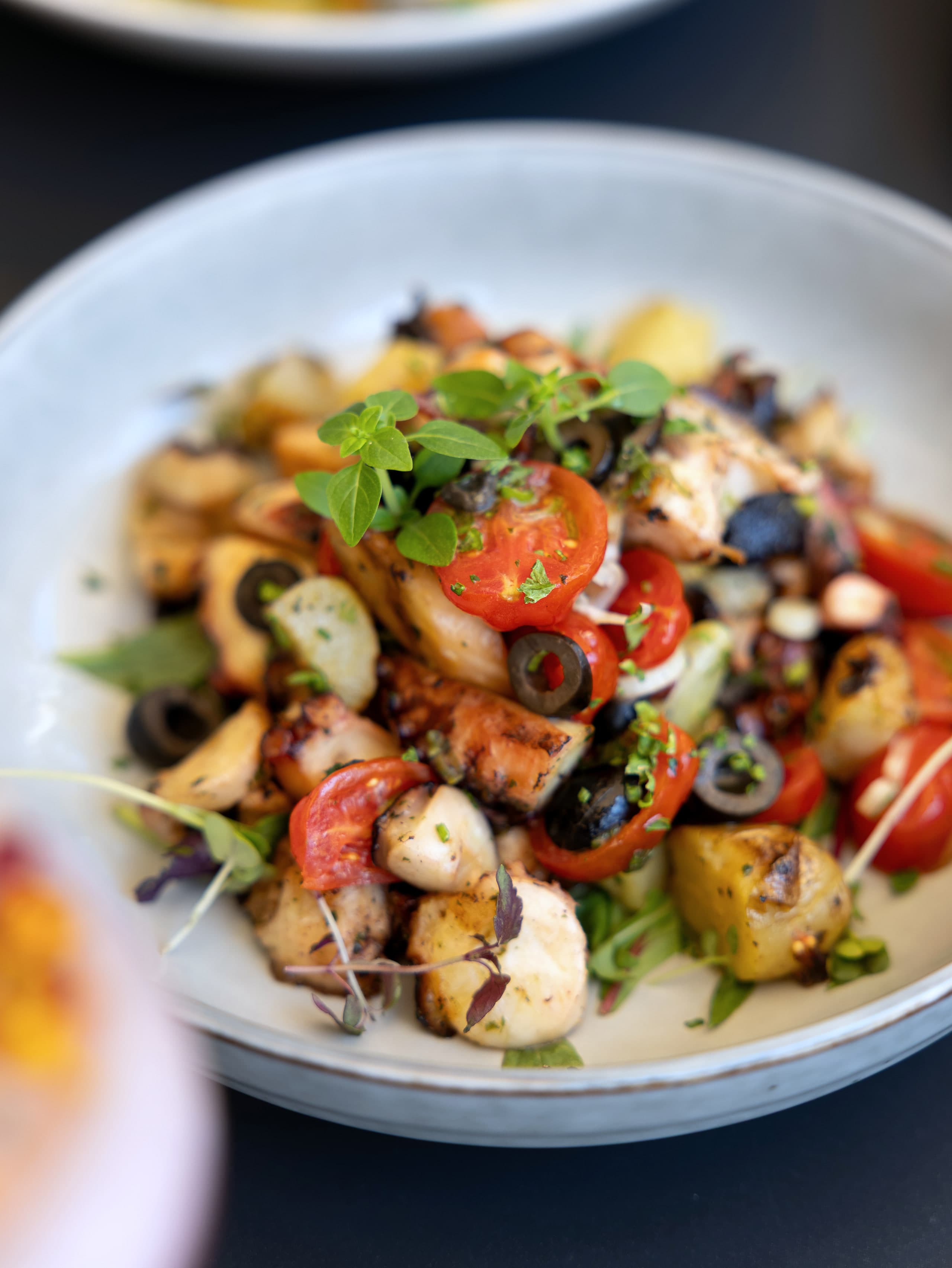 Salade de poulpe grillé, pommes de terre, tomates cerises, olives noires et origan frais dans un bol de grès