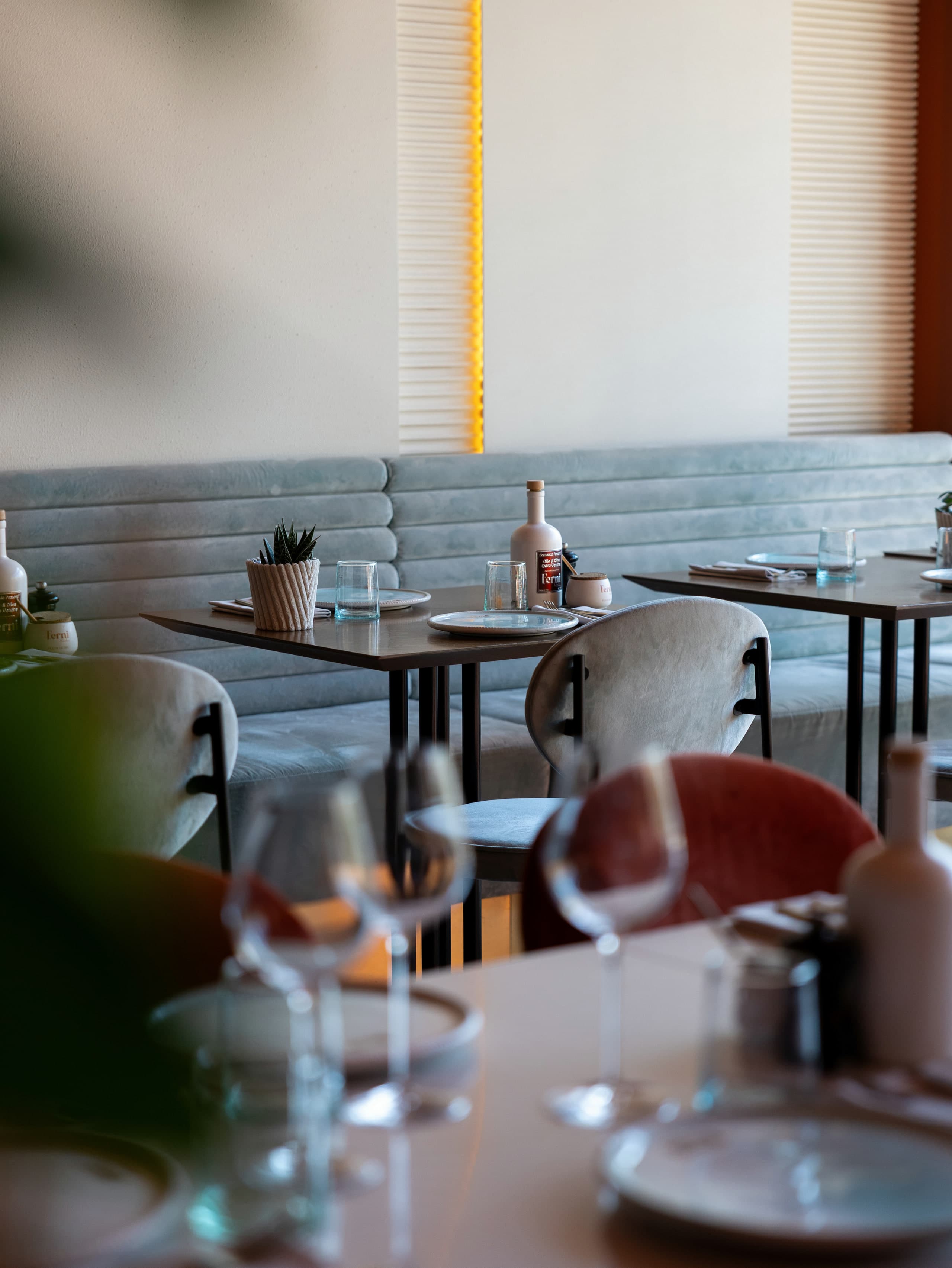 Deux tables carrées devant une banquette cannelée vert d’eau, panneau de bois strié et néon vertical au mur