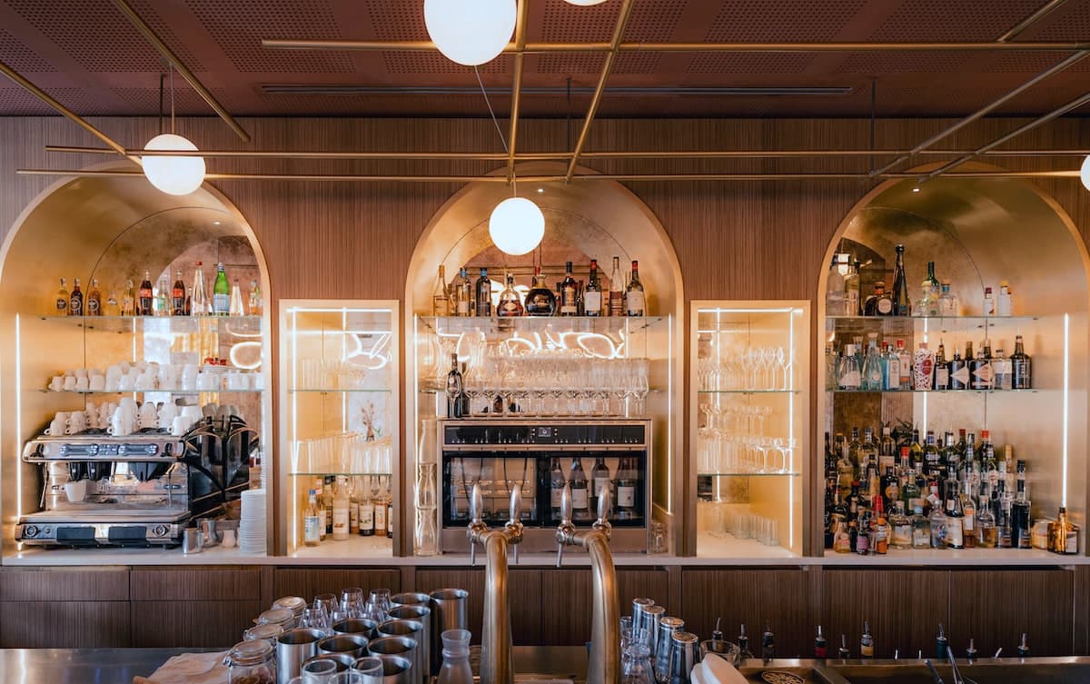 Le bar vu de face, trois niches voûtées garnies de bouteilles et de verrerie, machine à café sur la gauche