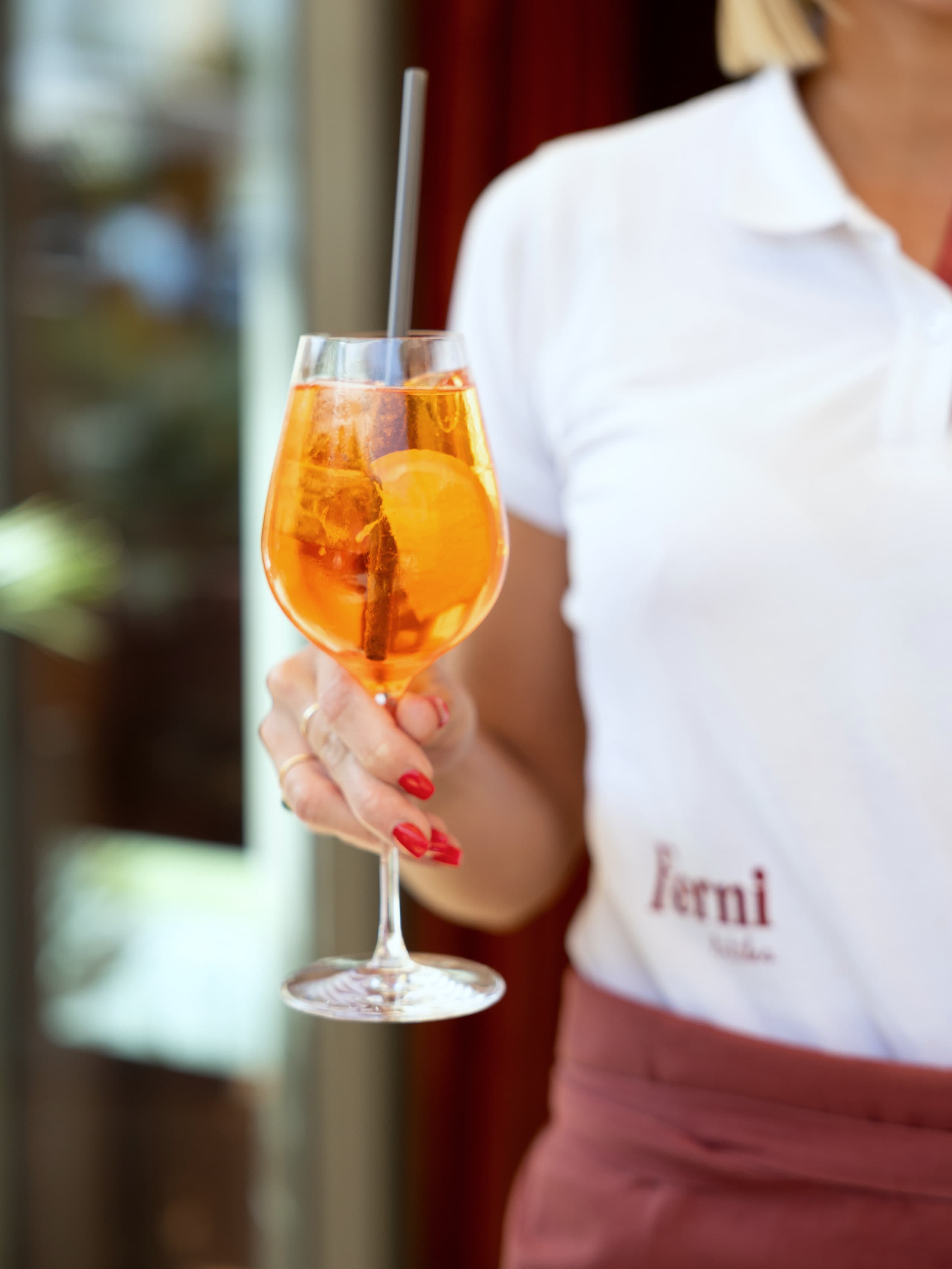 Spritz orange tenu à bout de bras par une serveuse en polo blanc brodé Ferni